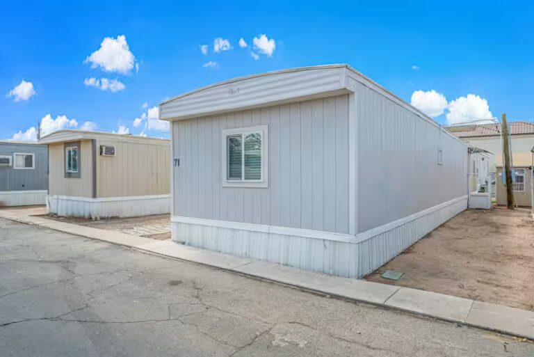 White mobile home numbered 71 with vertical siding under a blue sky with scattered clouds
