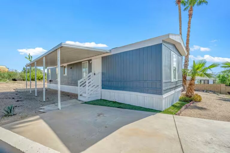 Single-wide manufactured home with white awning and concrete driveway beneath a clear desert sky.